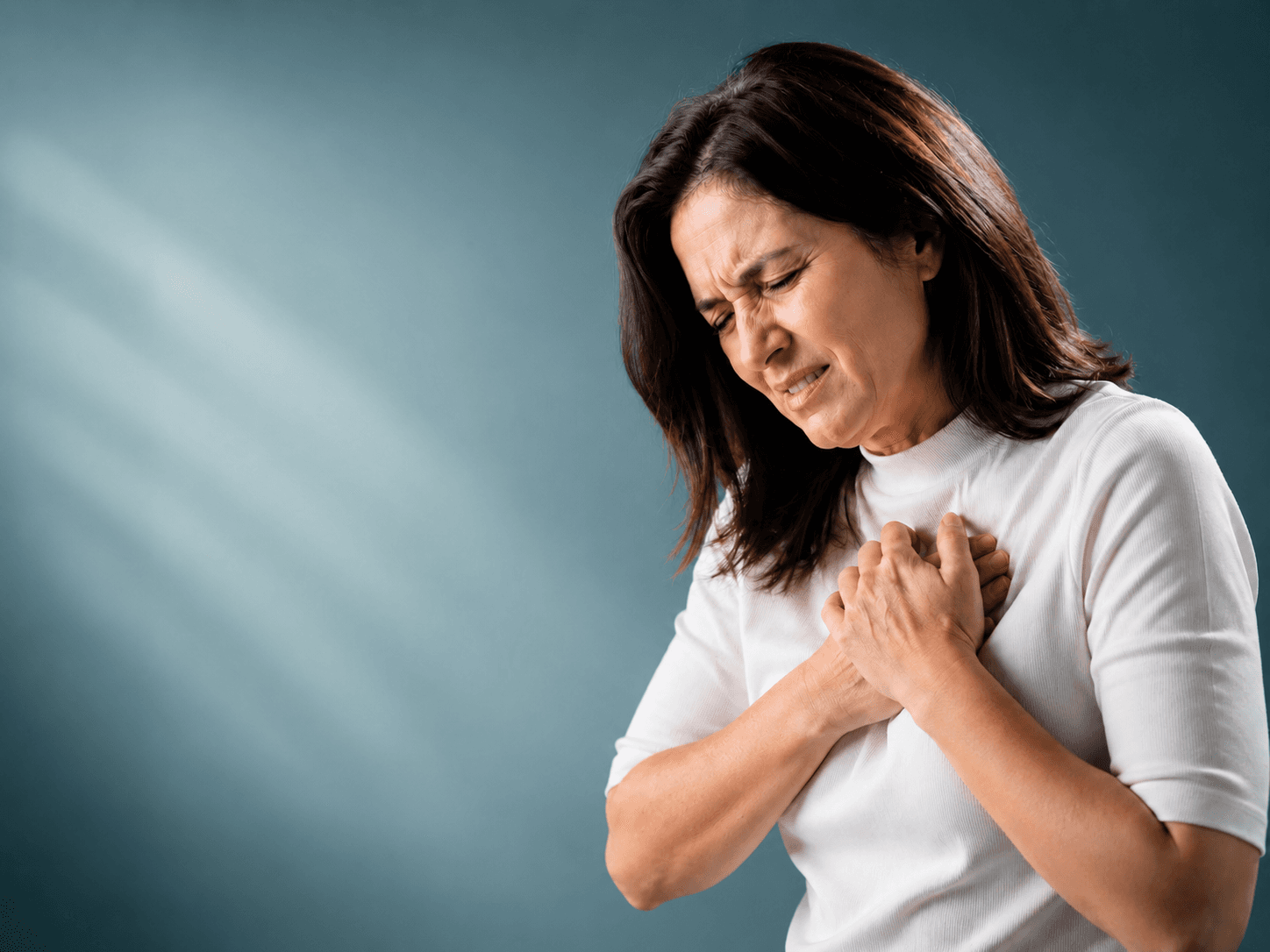Middle-aged woman holding chest due to heart pain, illustrating the link between long-term antibiotics, gut microbiome, and heart disease risk.